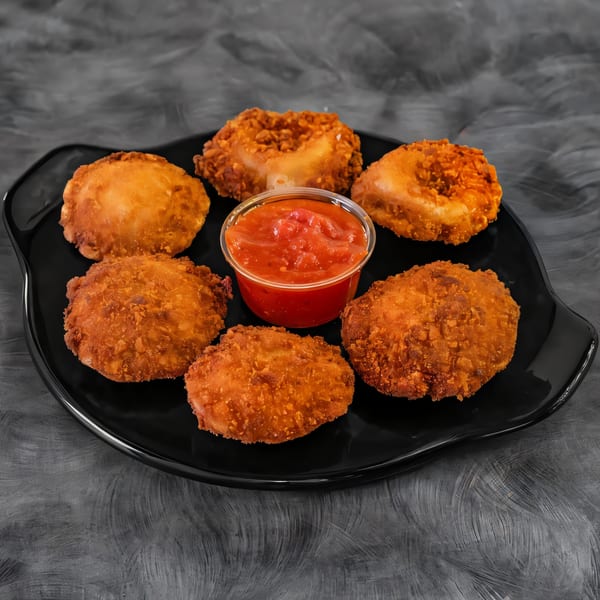 A black plate holds six golden-brown fried appetizers and a small cup of red marinara sauce.