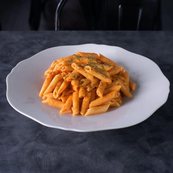 Penne pasta in a creamy orange sauce, topped with herbs, on a white plate.