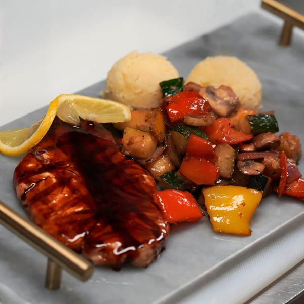 Grilled salmon with lemon, mashed potatoes, and sautéed vegetables on a marble tray.